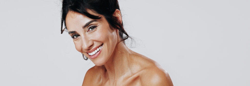 Smiling woman with dark hair and glowy skin posing against a white background.