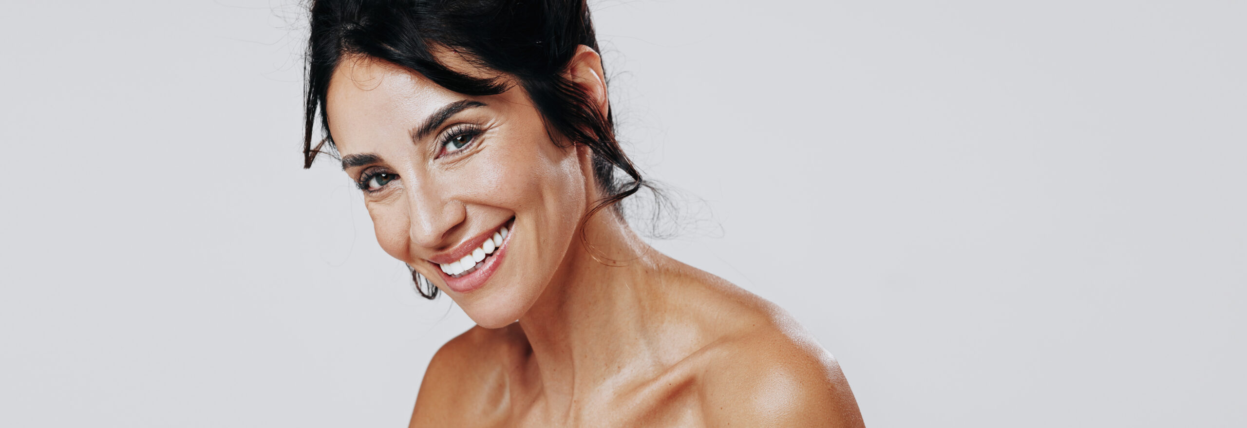 Smiling woman with dark hair and glowy skin posing against a white background.