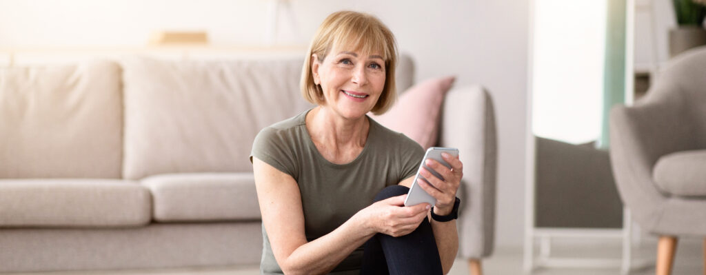 Smiling woman holding a smartphone in a bright living room.