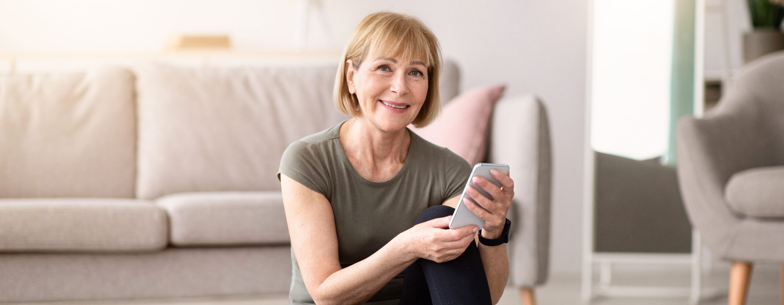 Smiling woman holding a smartphone in a bright living room.
