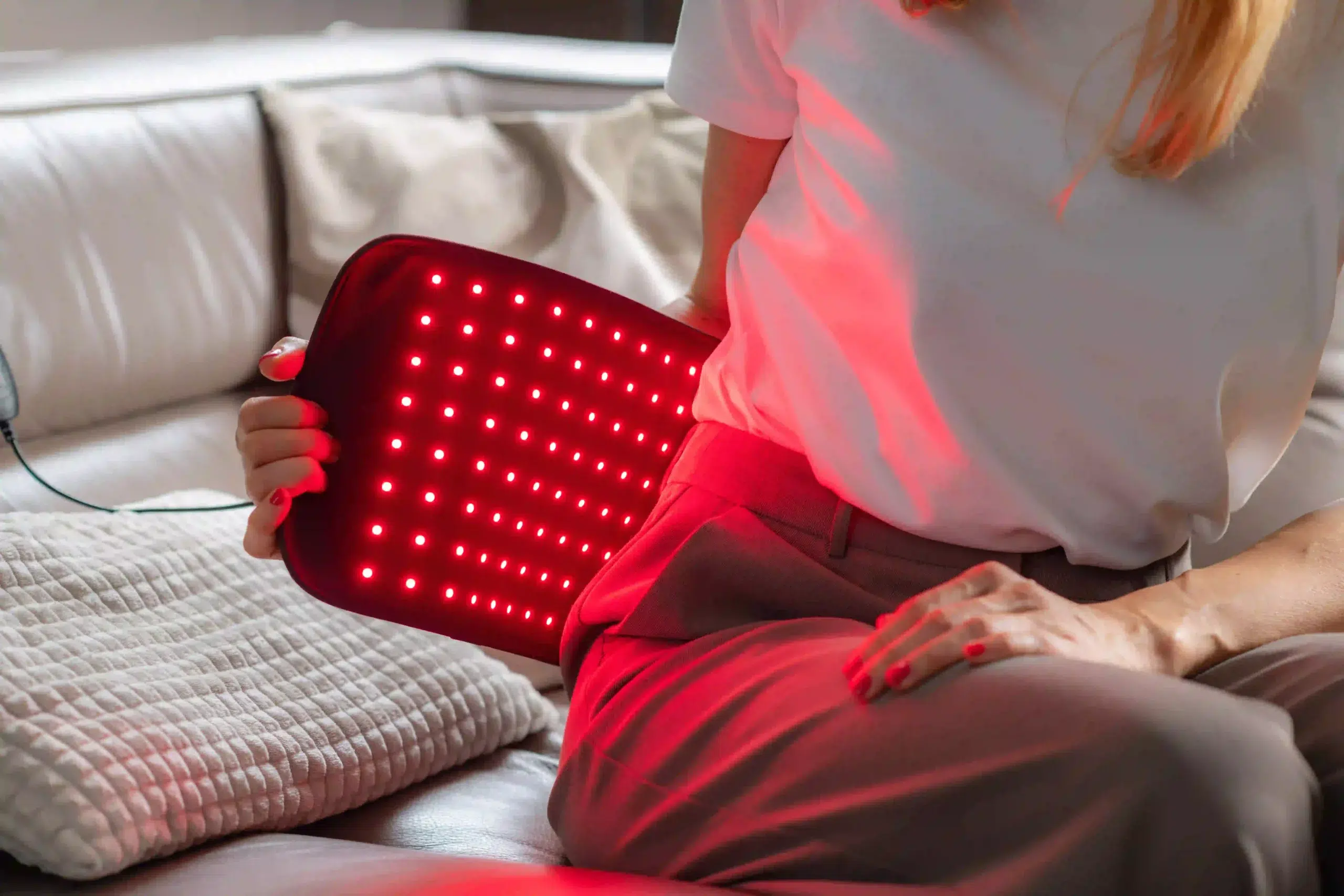 Woman applying a red light therapy heating pad to her lower back