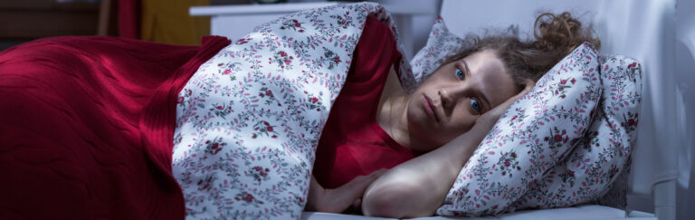Distressed young woman lying awake in bed at night, struggling with insomnia.
