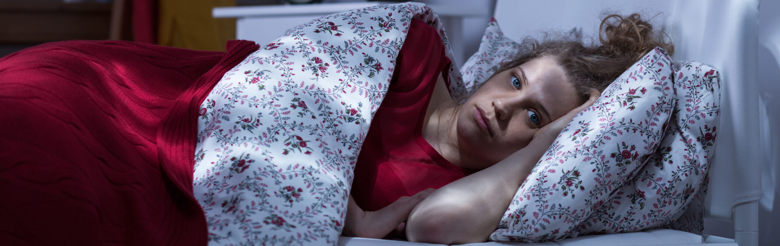 Distressed young woman lying awake in bed at night, struggling with insomnia.